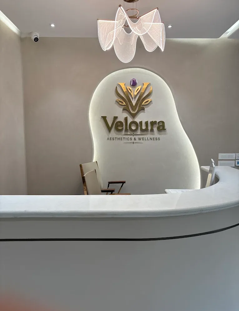 Veloura Clinic Gurgaon reception with a curved white counter and the gold Veloura logo wall